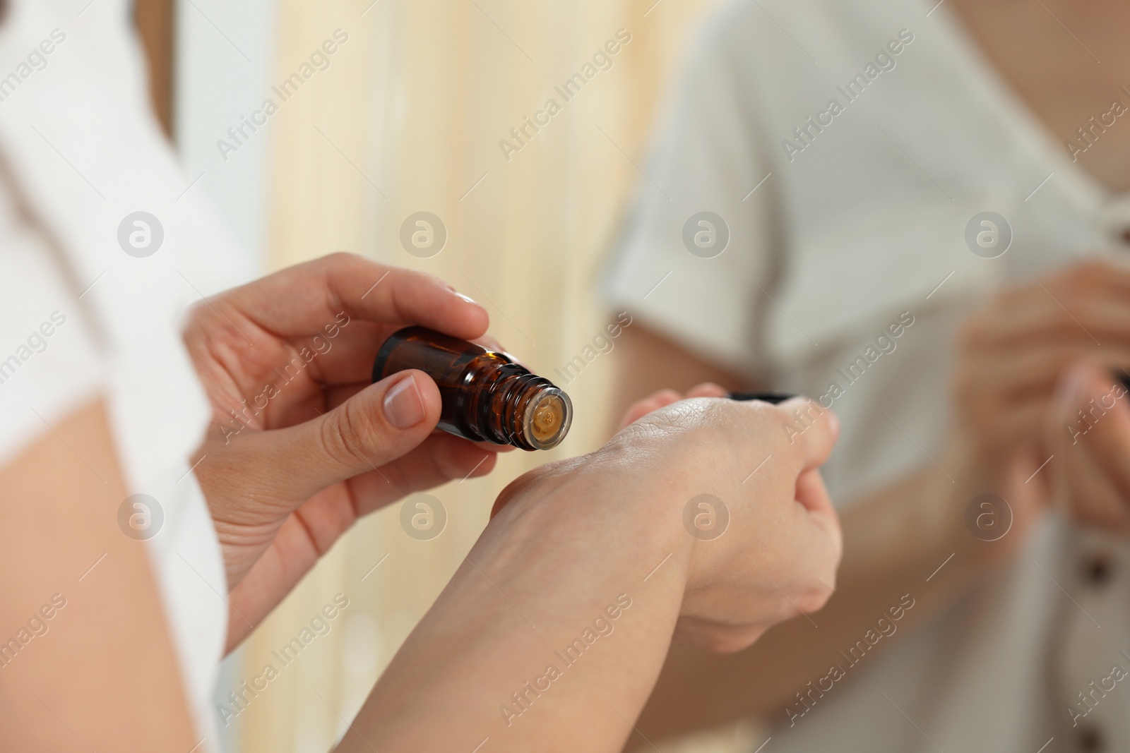 Photo of Young woman applying essential oil onto wrist on blurred background, closeup