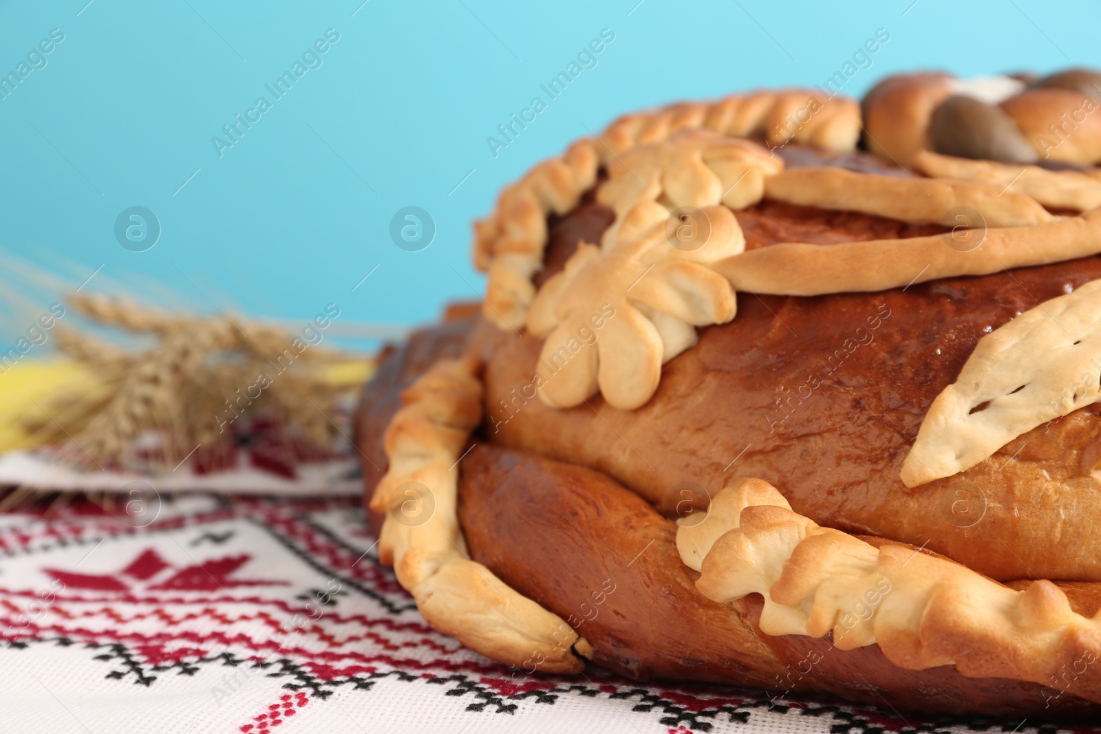 Photo of Rushnyk with korovai on table against light blue background, closeup. Ukrainian bread and salt welcoming tradition