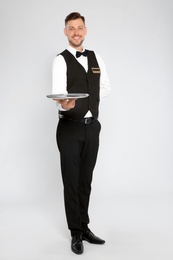 Photo of Handsome waiter with empty tray on light background