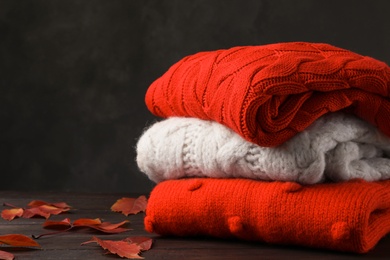 Photo of Stack of folded knitted sweaters and autumn leaves on table. Space for text