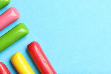 Photo of Many tasty bubble gums on light blue background, flat lay. Space for text