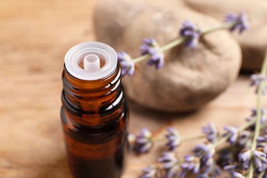 Photo of Bottle of essential oil and lavender flowers on wooden table, closeup. Space for text