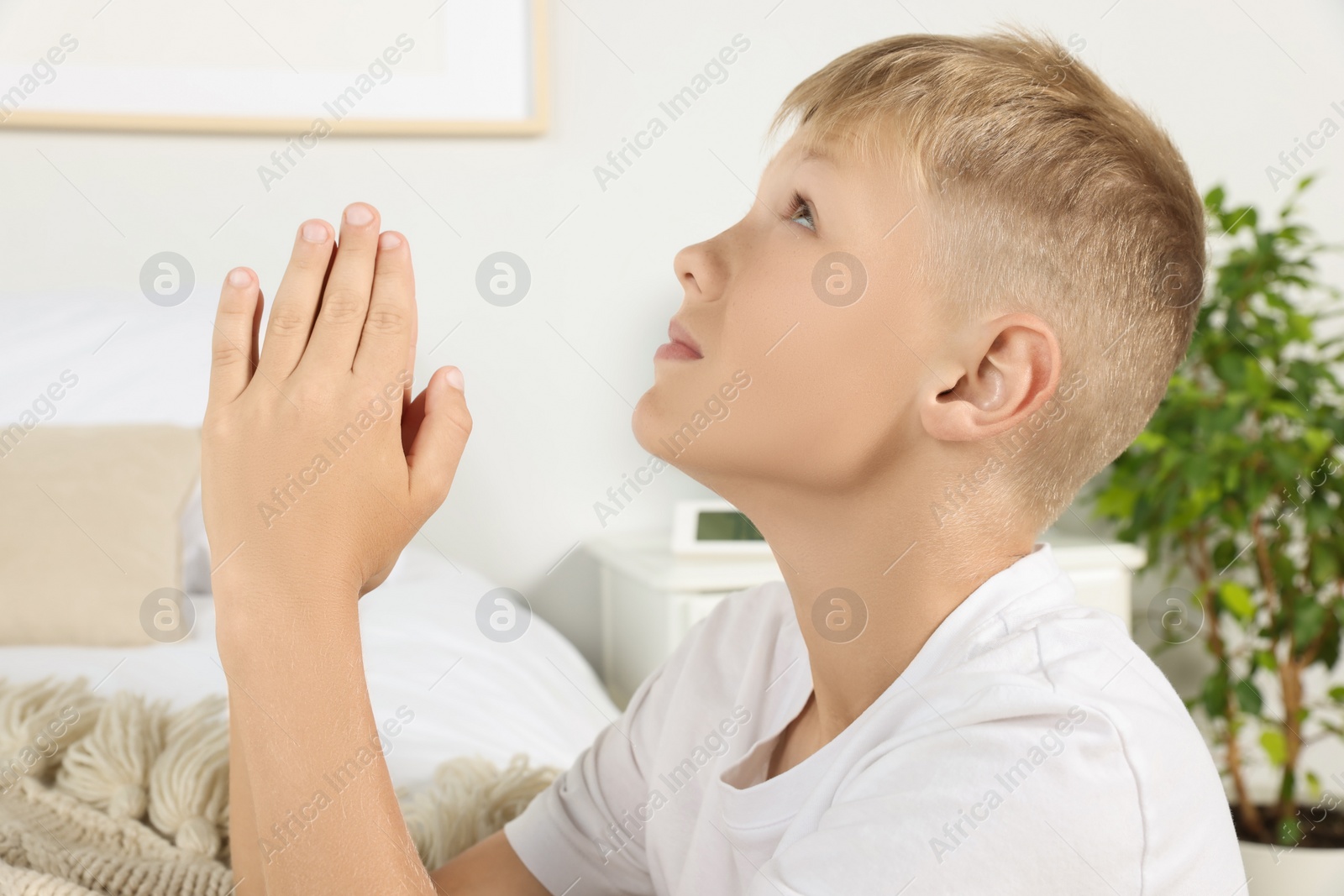 Photo of Boy with clasped hands praying near bed at home