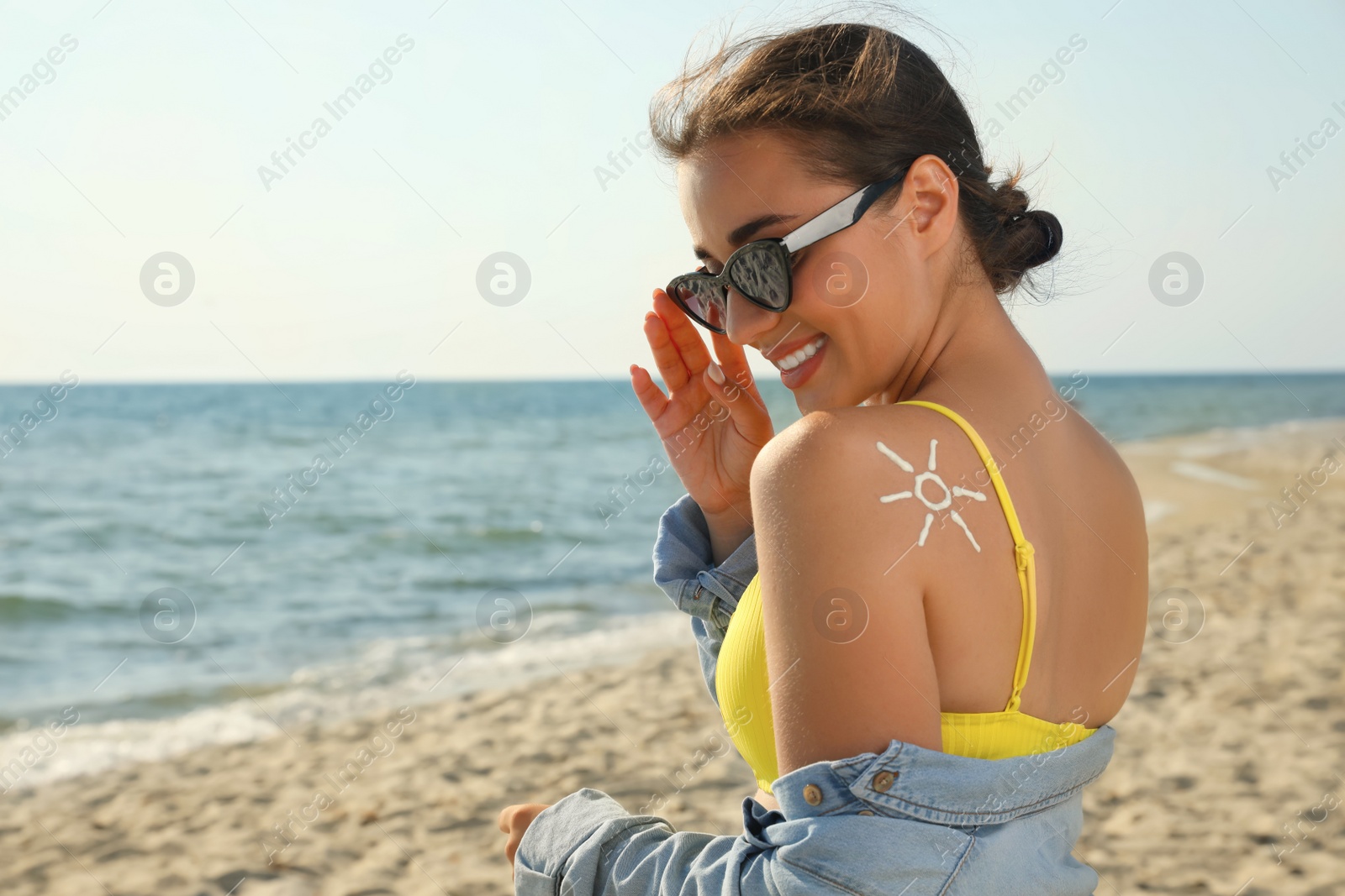 Photo of Beautiful young woman with sun protection cream on shoulder at beach