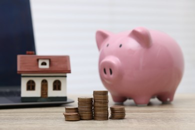 Photo of House model, piggy bank and stacked coins on light wooden table, selective focus