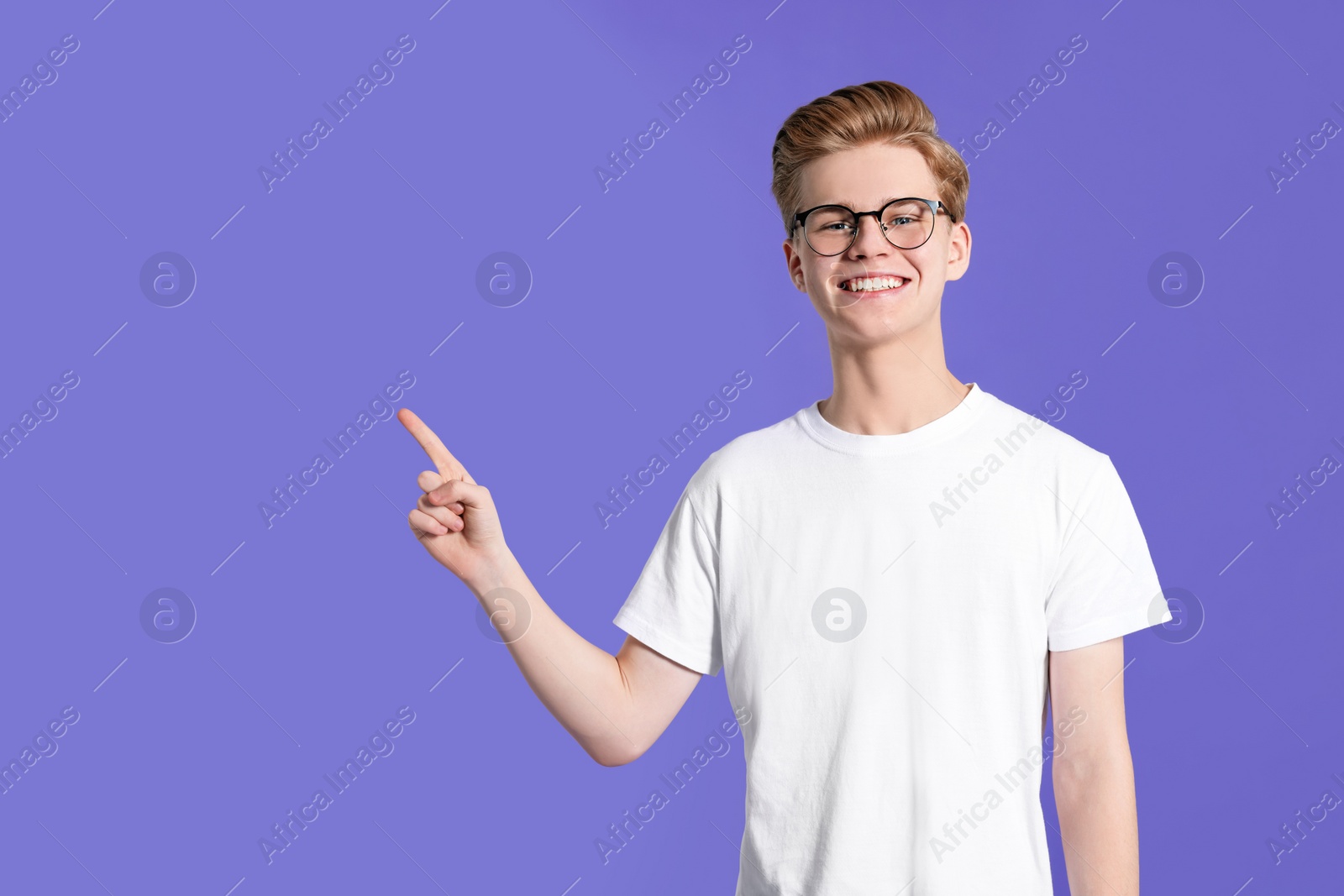 Photo of Teenage boy pointing at something on purple background. Space for text