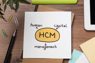 Paper with HCM abbreviation on wooden office table, flat lay. Human Capital Management