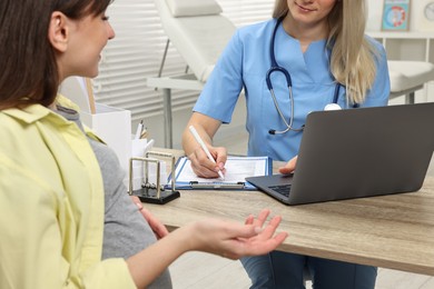 Doctor consulting pregnant woman at table in clinic, closeup