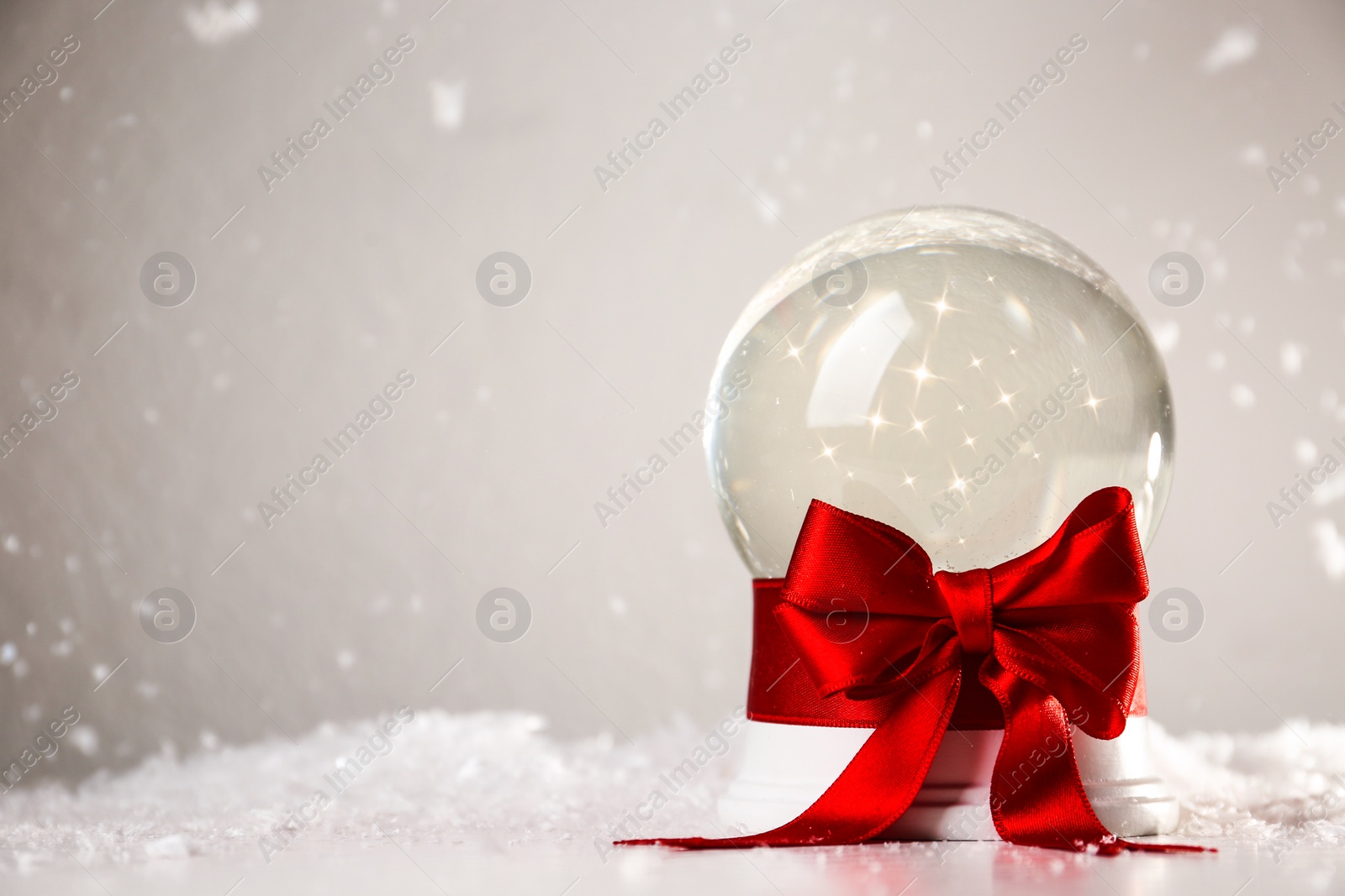 Photo of Beautiful Christmas snow globe with red bow on table against light background, space for text