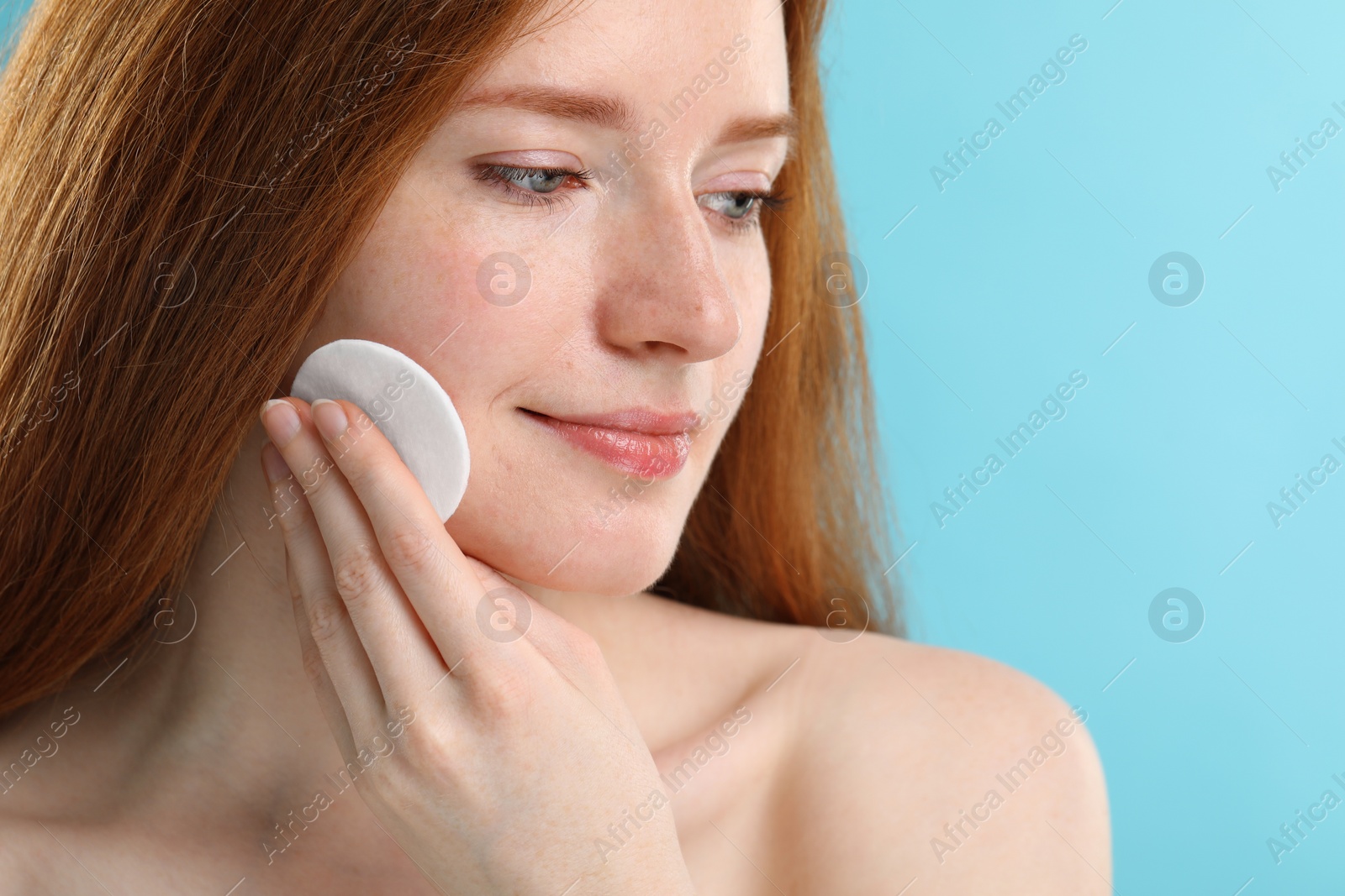 Photo of Beautiful woman with freckles wiping face on light blue background, closeup. Space for text