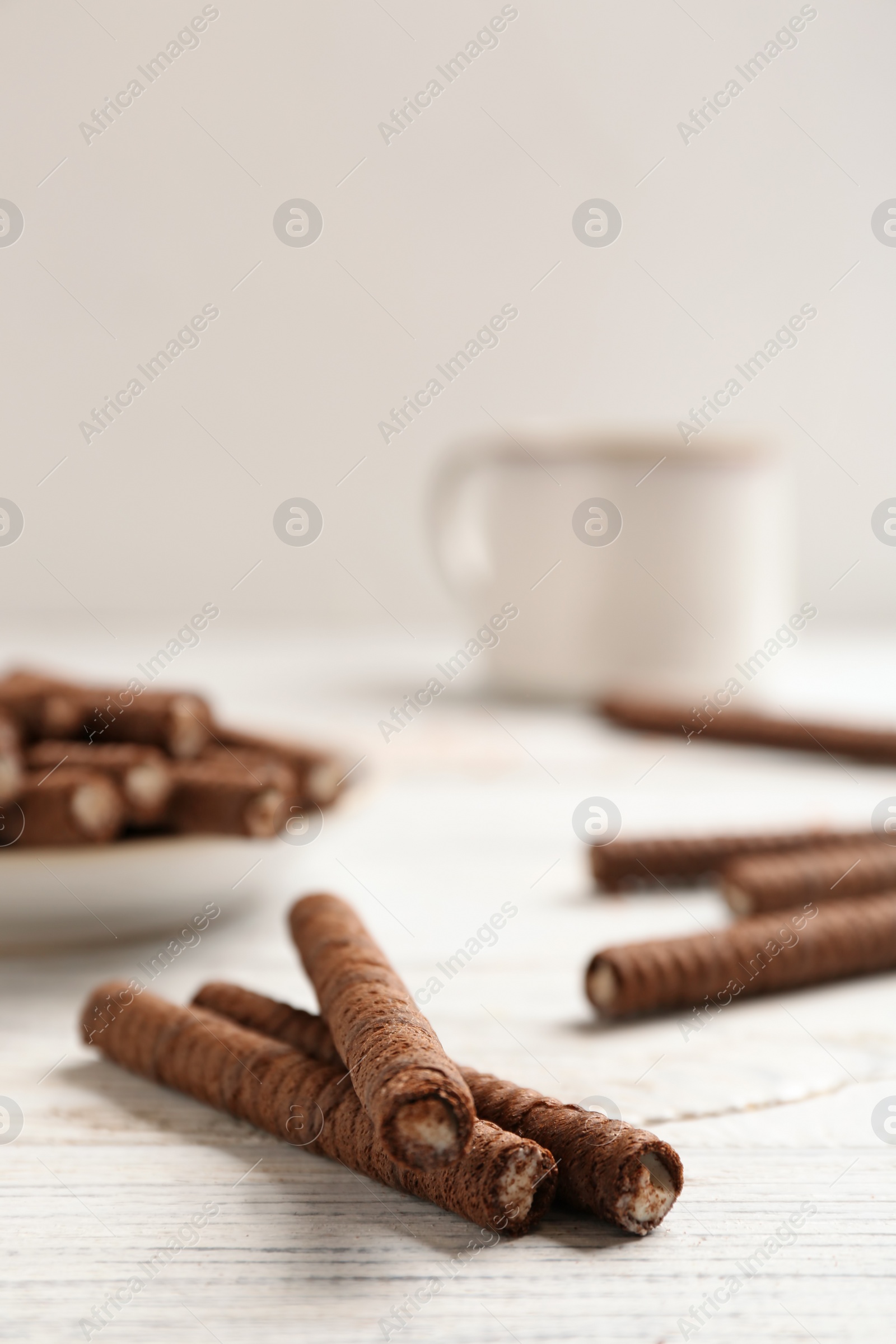 Photo of Delicious chocolate wafer rolls on white wooden table, space for text. Sweet food