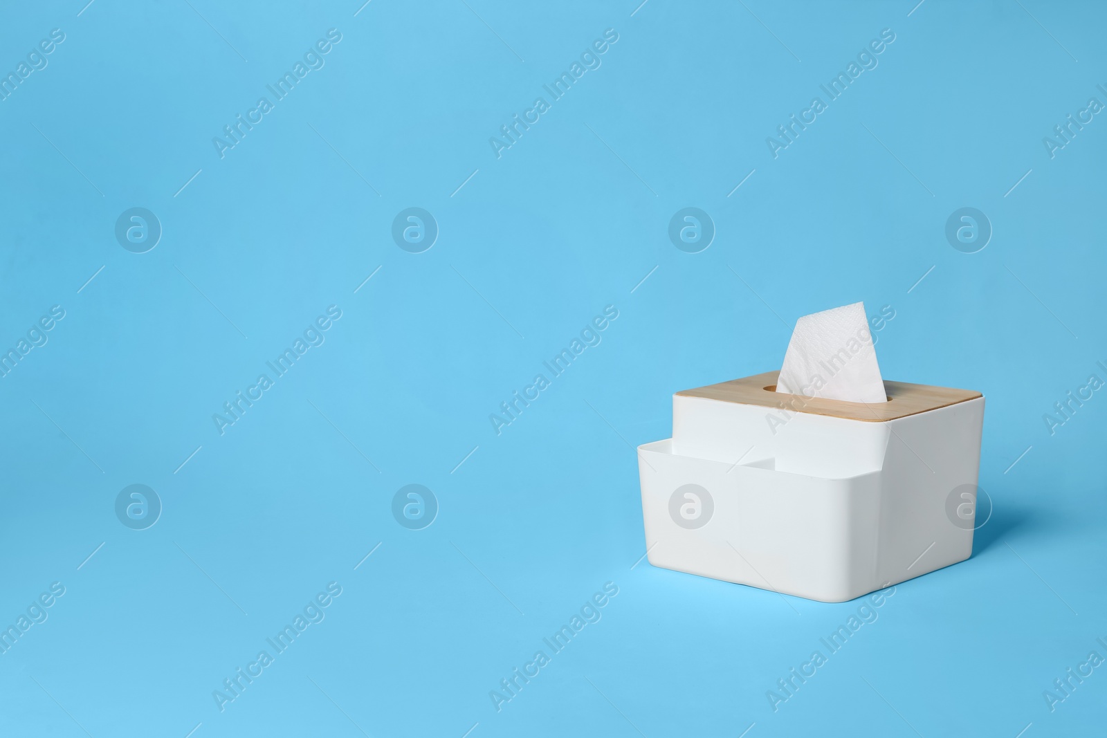 Photo of Holder with paper tissues on light blue background. Space for text