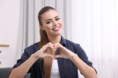 Photo of Happy woman showing heart gesture with hands at home