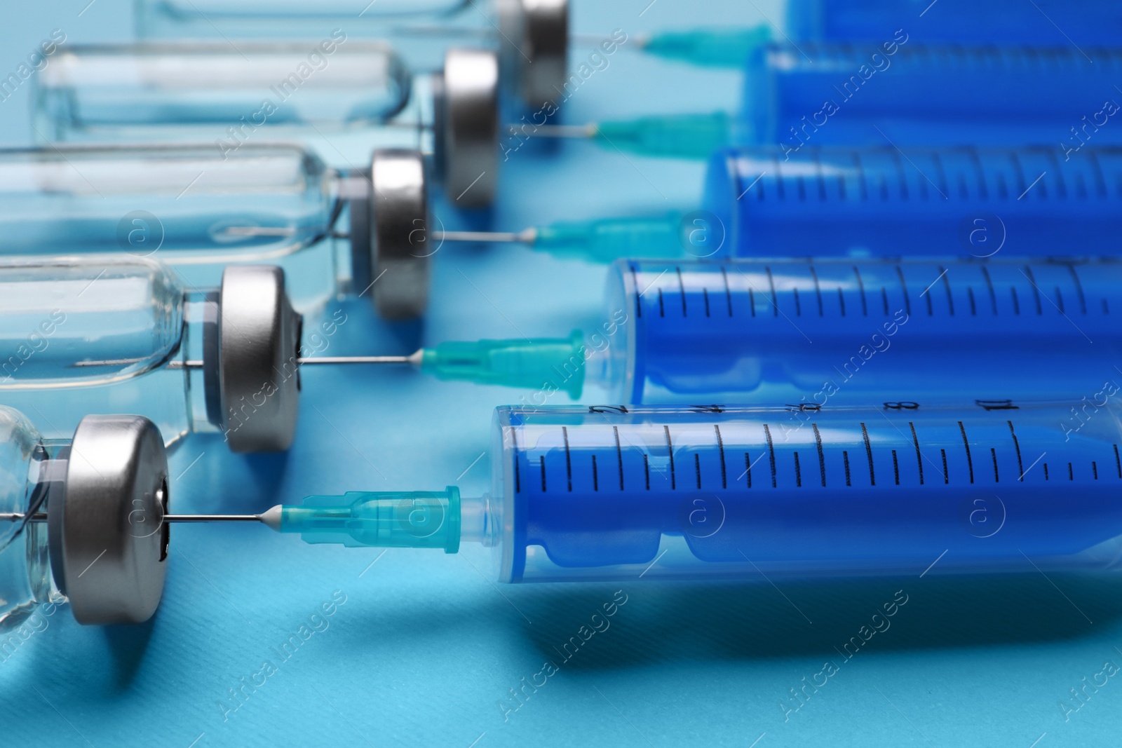 Photo of Disposable syringes with needles and vials on light blue background, closeup
