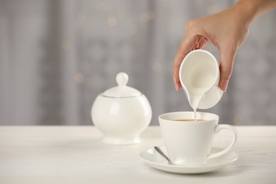 Photo of Woman pouring milk into cup with coffee at table indoors, closeup