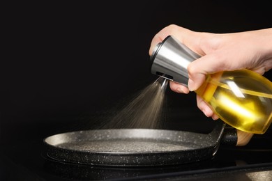 Photo of Woman spraying cooking oil onto frying pan on stove, closeup