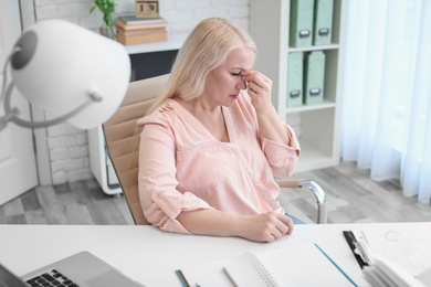 Photo of Mature woman suffering from headache while sitting at table in office