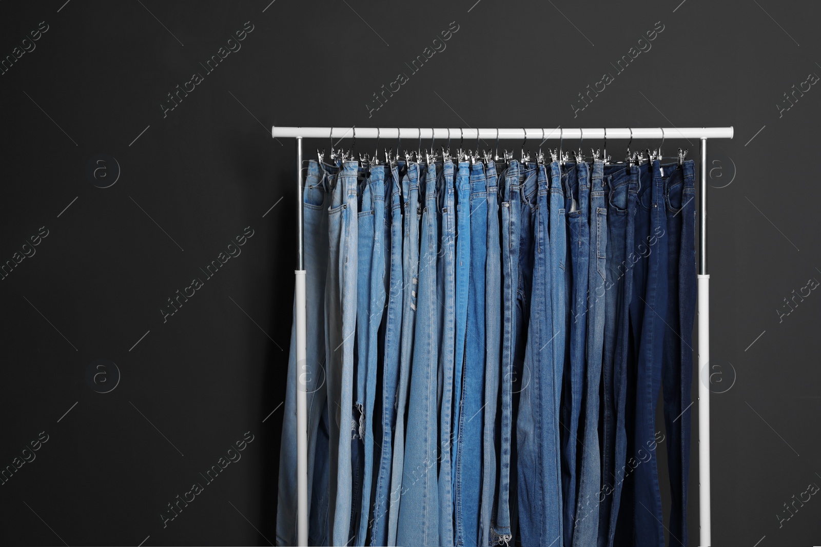 Photo of Rack with different jeans on dark grey background