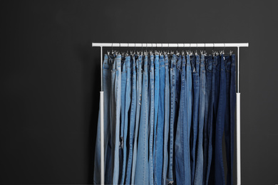 Photo of Rack with different jeans on dark grey background