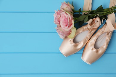 Photo of Beautiful beige ballet shoes with cute ribbons and rose flowers on light blue wooden table, flat lay. Space for text