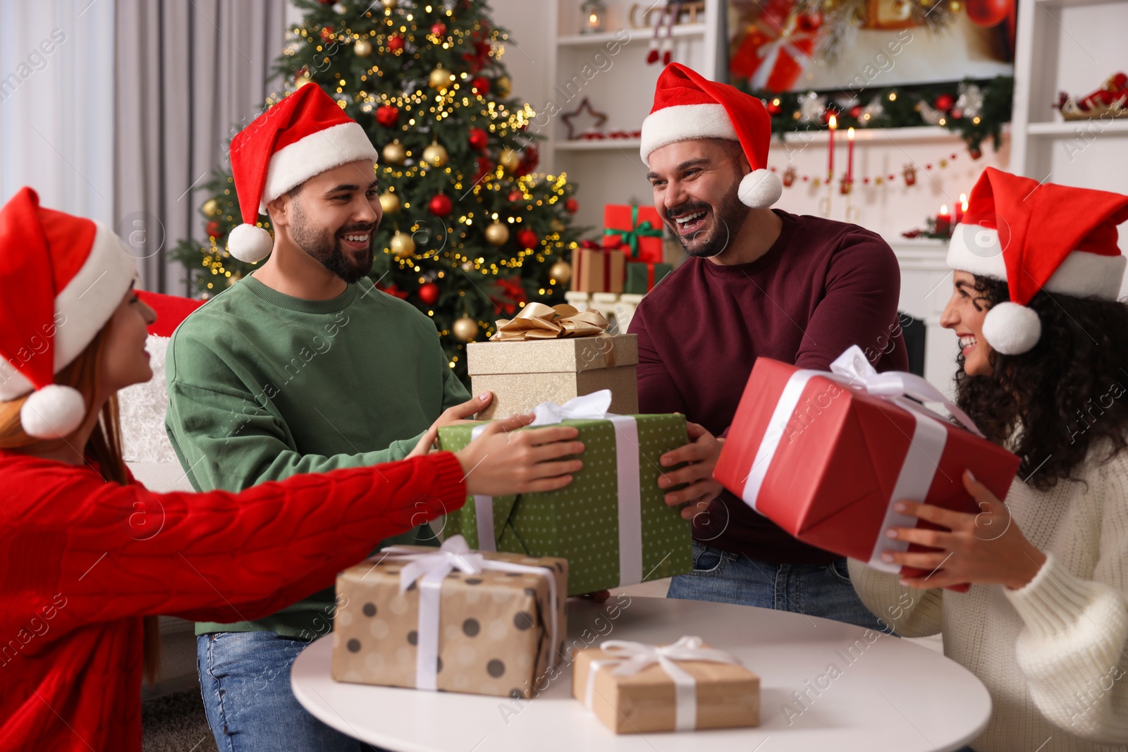 Photo of Christmas celebration. Happy friends in Santa hats exchanging gifts at home