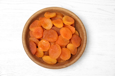 Photo of Wooden bowl with dried apricots on white table, top view. Healthy fruit
