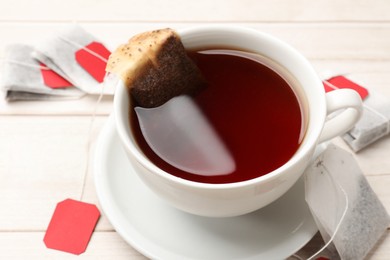 Tea bags and cup of hot beverage on light wooden table, closeup