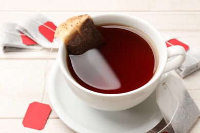 Photo of Tea bags and cup of hot beverage on light wooden table, closeup