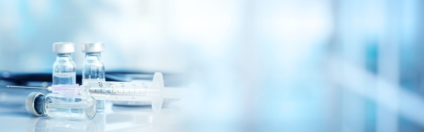 Syringe, glass vials and stethoscope on table against blurred background, space for text. Banner design