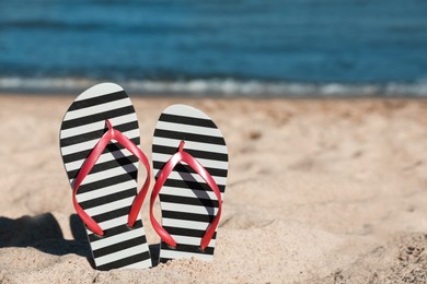 Striped flip flops in sand on beach near sea. Space for text