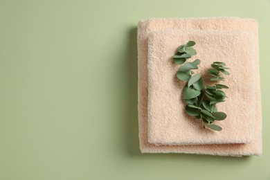 Photo of Soft folded towels with eucalyptus branch on green background, top view. Space for text
