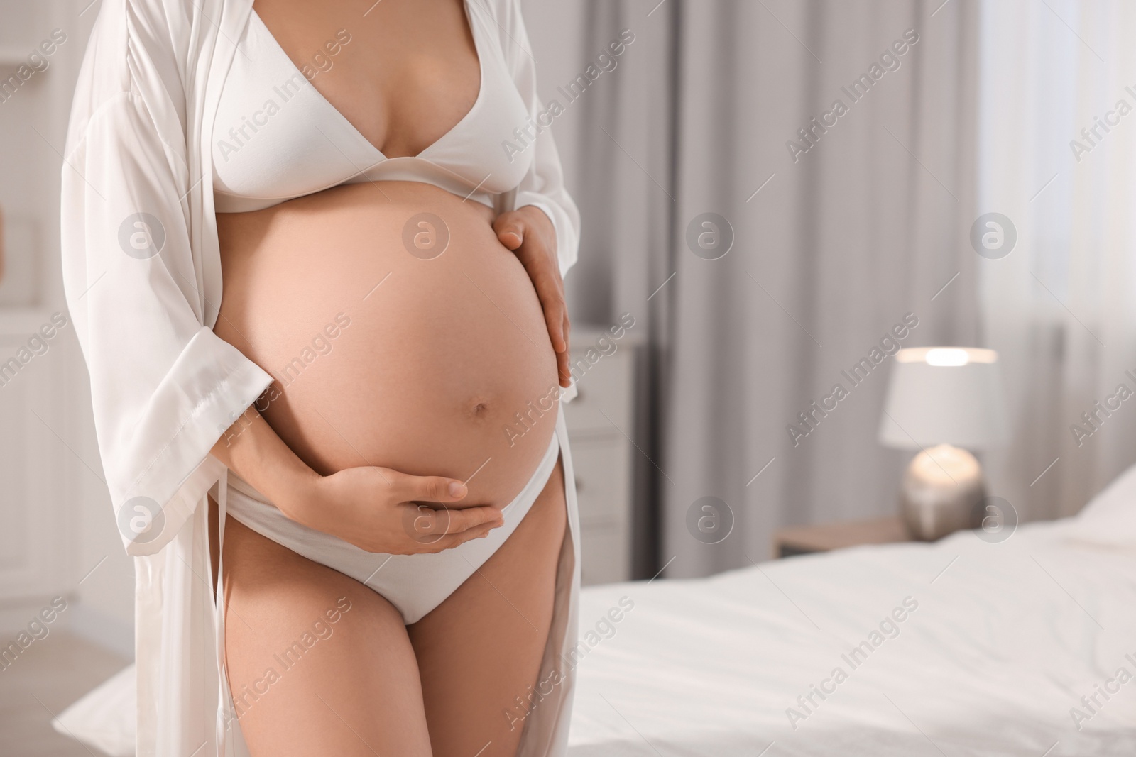 Photo of Pregnant woman wearing stylish comfortable underwear and robe in bedroom, closeup. Space for text