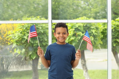 Photo of Happy African-American boy holding national flags near window indoors