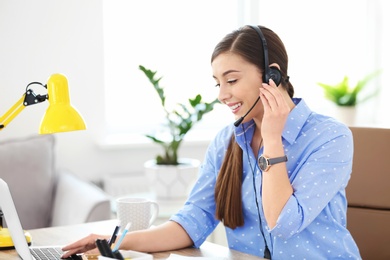 Photo of Young woman talking on phone through headset at workplace