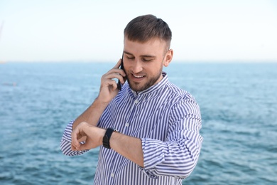 Photo of Portrait of handsome young man talking on phone near sea