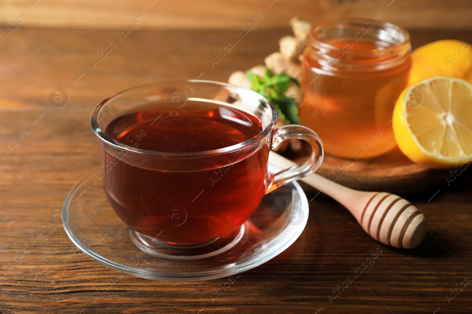 Photo of Cup of delicious ginger tea and ingredients on wooden table, closeup