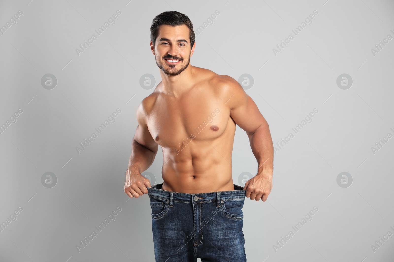 Photo of Young man with slim body in old big size jeans on grey background