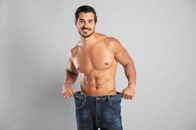 Photo of Young man with slim body in old big size jeans on grey background