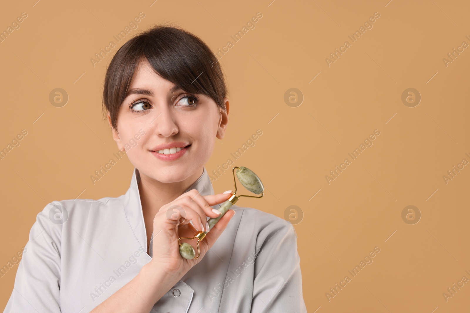 Photo of Cosmetologist with facial roller on beige background, space for text