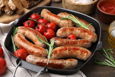 Photo of Grill pan with tasty homemade sausages, rosemary and tomatoes on wooden table, closeup