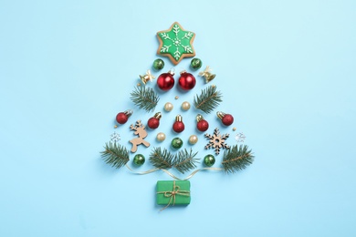 Photo of Christmas tree silhouette of fir branches and festive decoration on light blue background, flat lay