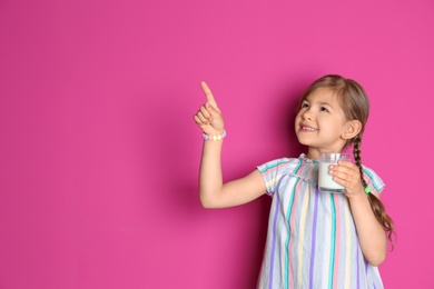 Cute little girl with glass of milk on color background