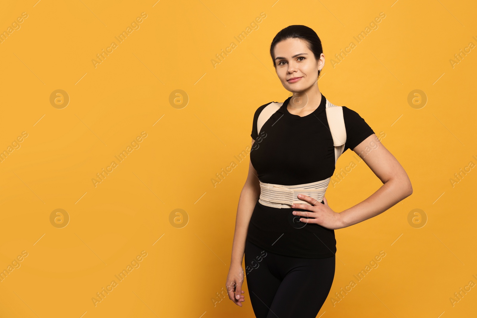 Photo of Beautiful woman with orthopedic corset on orange background, space for text