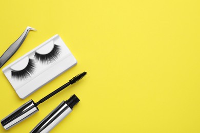 Flat lay composition with fake eyelashes, mascara brush and tweezers on yellow background. Space for text