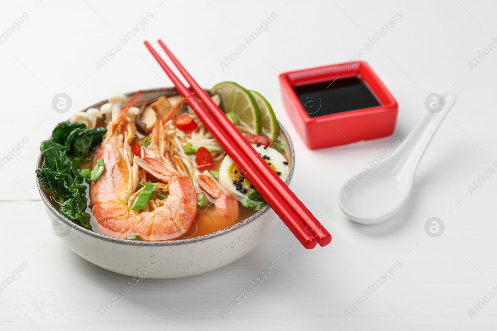 Photo of Delicious ramen with shrimps and egg in bowl served on white wooden table. Noodle soup