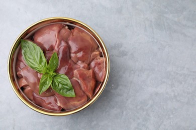 Photo of Bowl with raw chicken liver and basil on light grey table, top view. Space for text