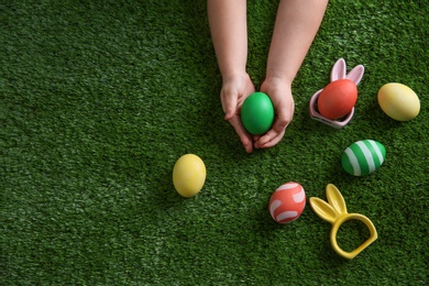 Photo of Little child holding painted Easter egg on green grass, top view. Space for text