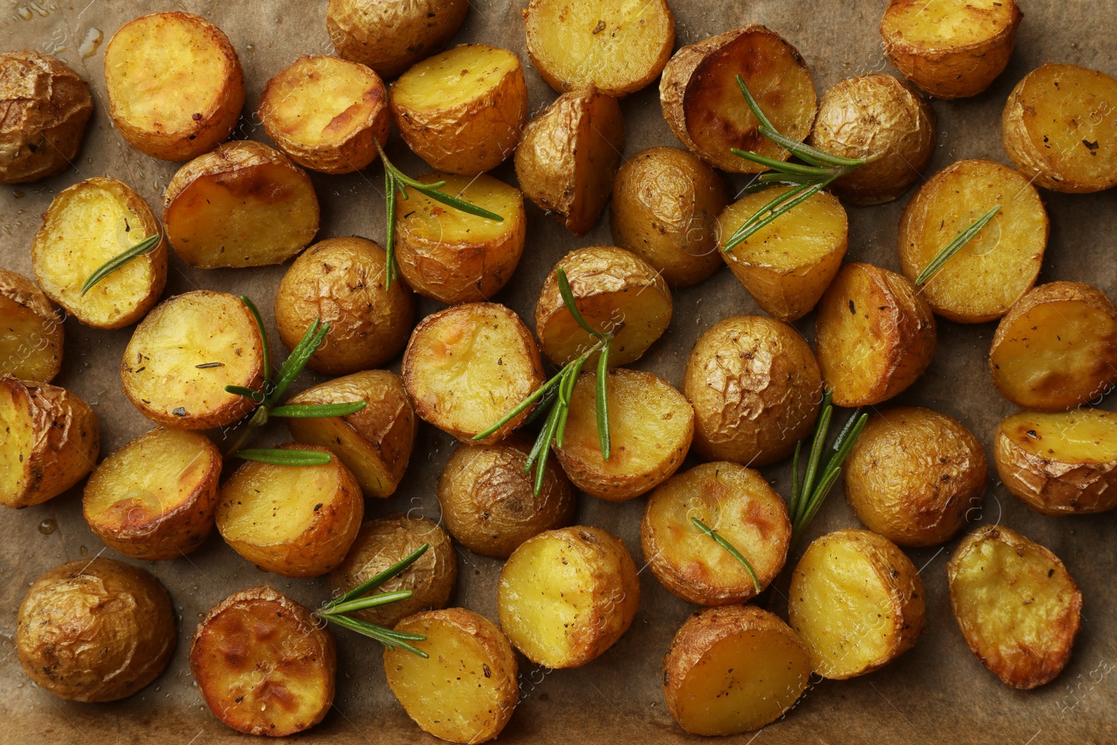 Photo of Tasty baked potato and aromatic rosemary on parchment paper, flat lay