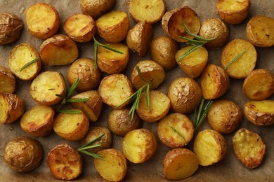 Photo of Tasty baked potato and aromatic rosemary on parchment paper, flat lay