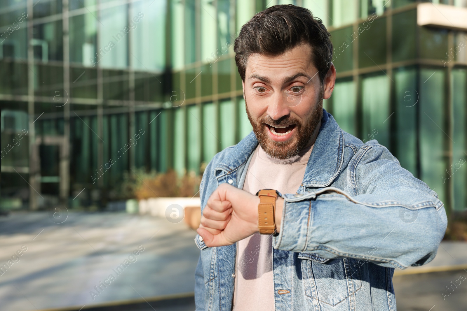 Photo of Emotional man checking time on watch near building. Being late concept